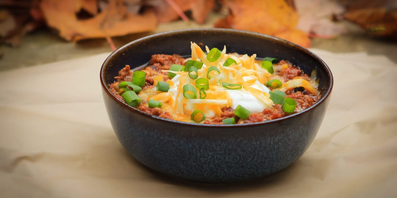 A bowl of chili with cheese and green onions.